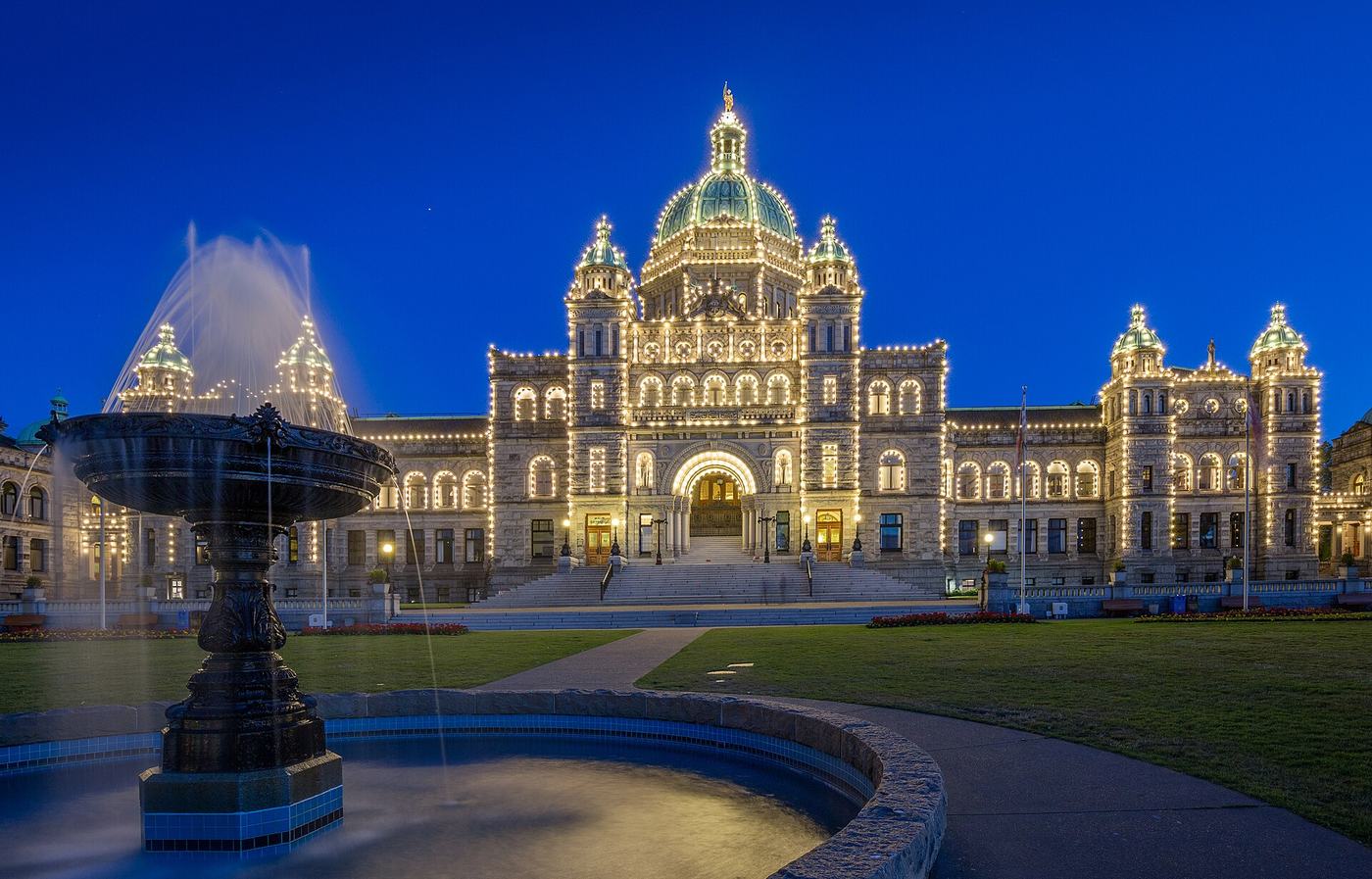 The British Columbia Parliament Buildings lit up at night in Victoria, with the fountain in the foreground